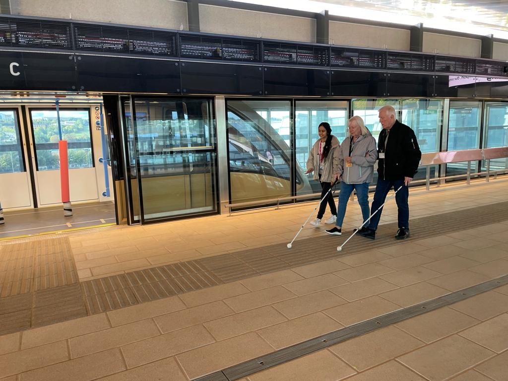Image shows three Bedfordshire SLC members walking on the platform, alongside the DART Shuttle train. Two members are walking with their white canes.