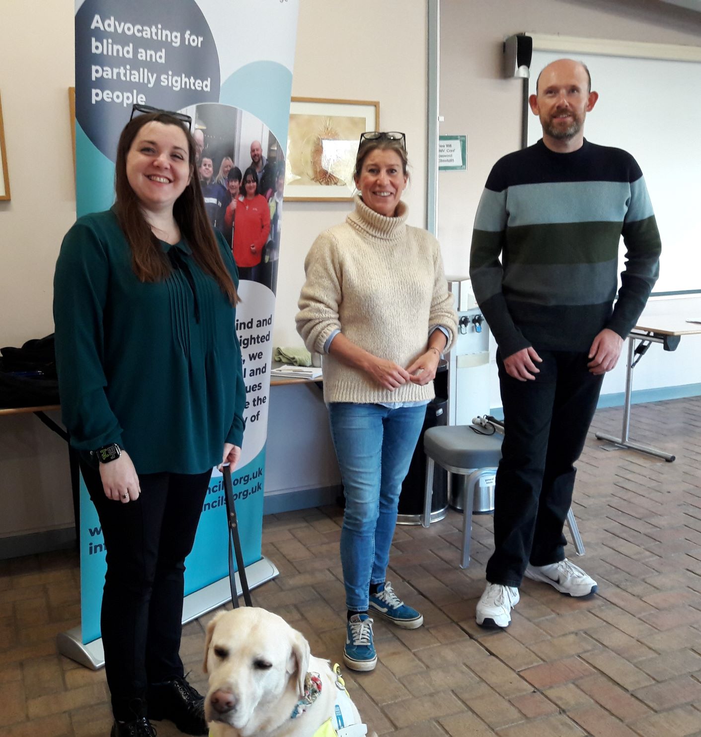 From left to right: Bedfordshire Engagement Manager, Sam Leftwich, Jo Roberts, Community Manager at Marston Vale, and SLC member Stefan Cocker. are standing by the SL banner, with guide dog Lizzie.