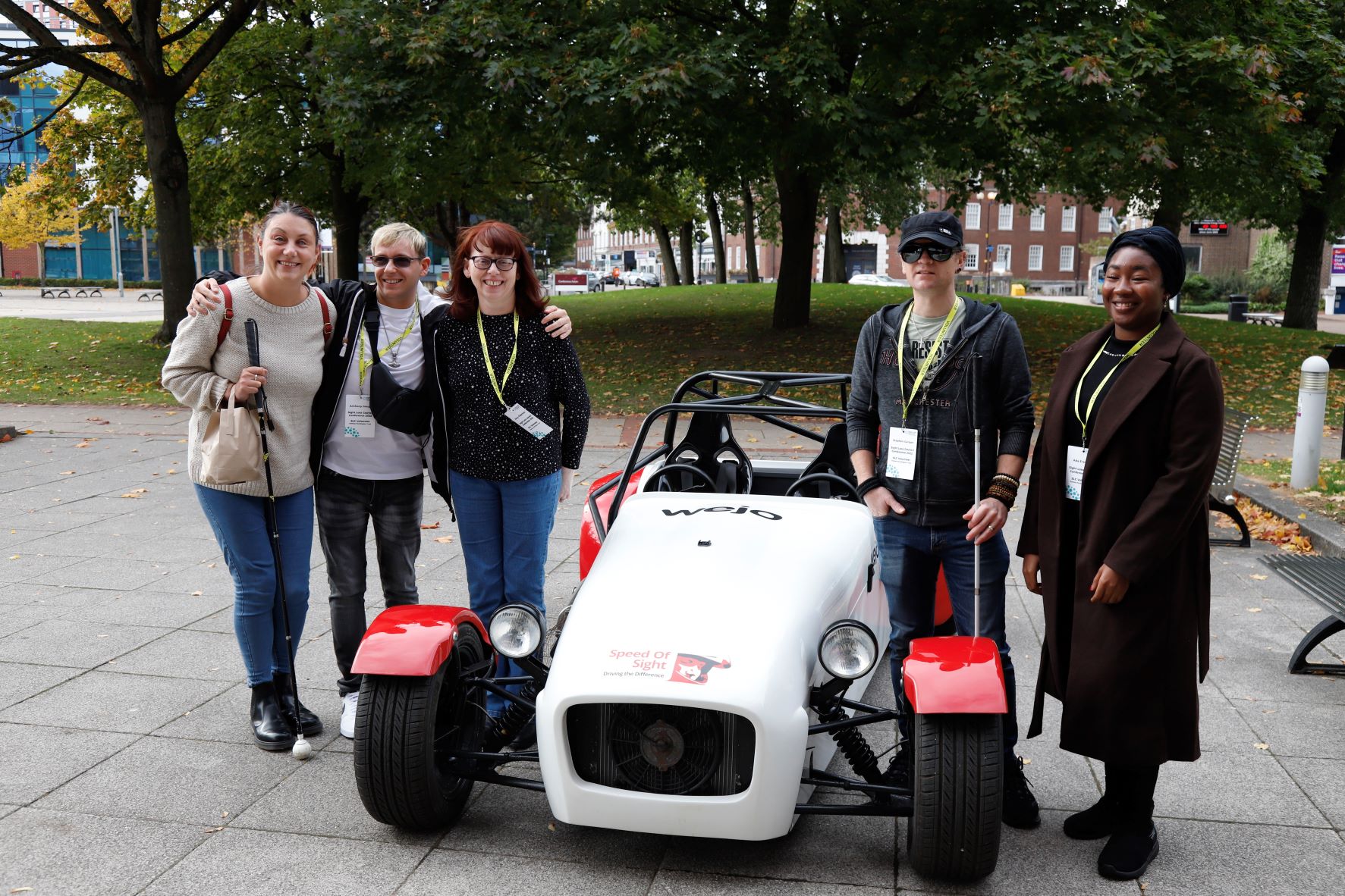 Five delegates standing either side of one of Mike's 'Speed of Sight' race cars. The car is white, with red wheel arches.