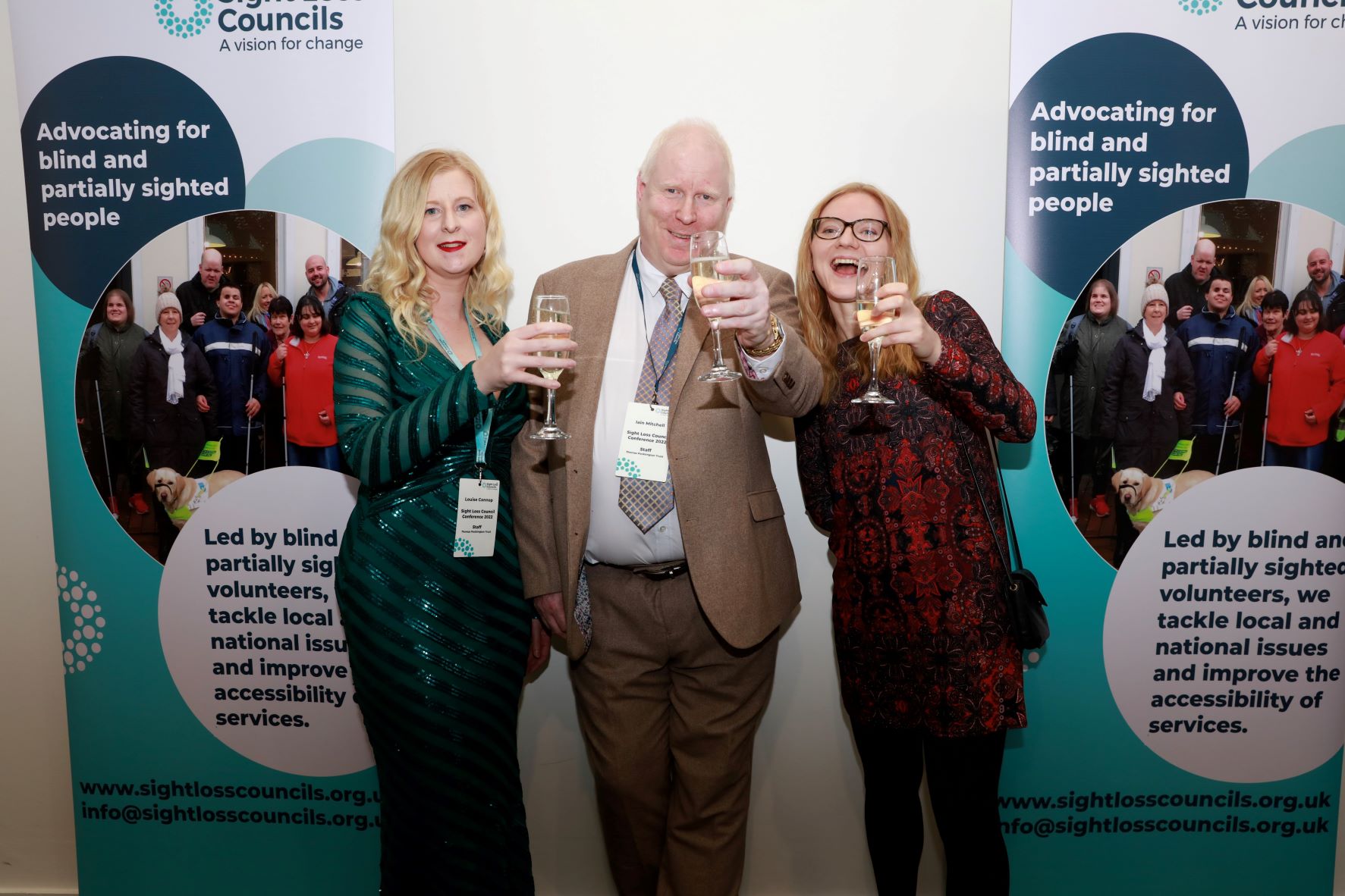 Left to right: Louise Connop, Senior Engagement Manager, Central region, Iain Mitchell, Senior Engagement Manager for the North, and Lucy Williams, Senior Engagement manager for the south. They are standing in front of a SLC banner, dressed up for the RPA awards. They are all holding a glass of fizz up towards the camera, smiling.