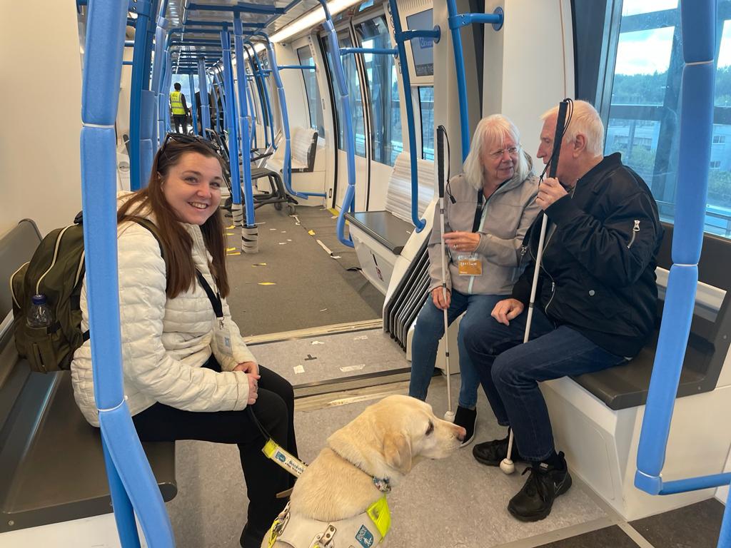 Image shows Engagement Manager, Sam Leftwich, sitting on the DART shuttle with guide dog Lizzie, and two members of Bedfordshire Sight Loss Council.