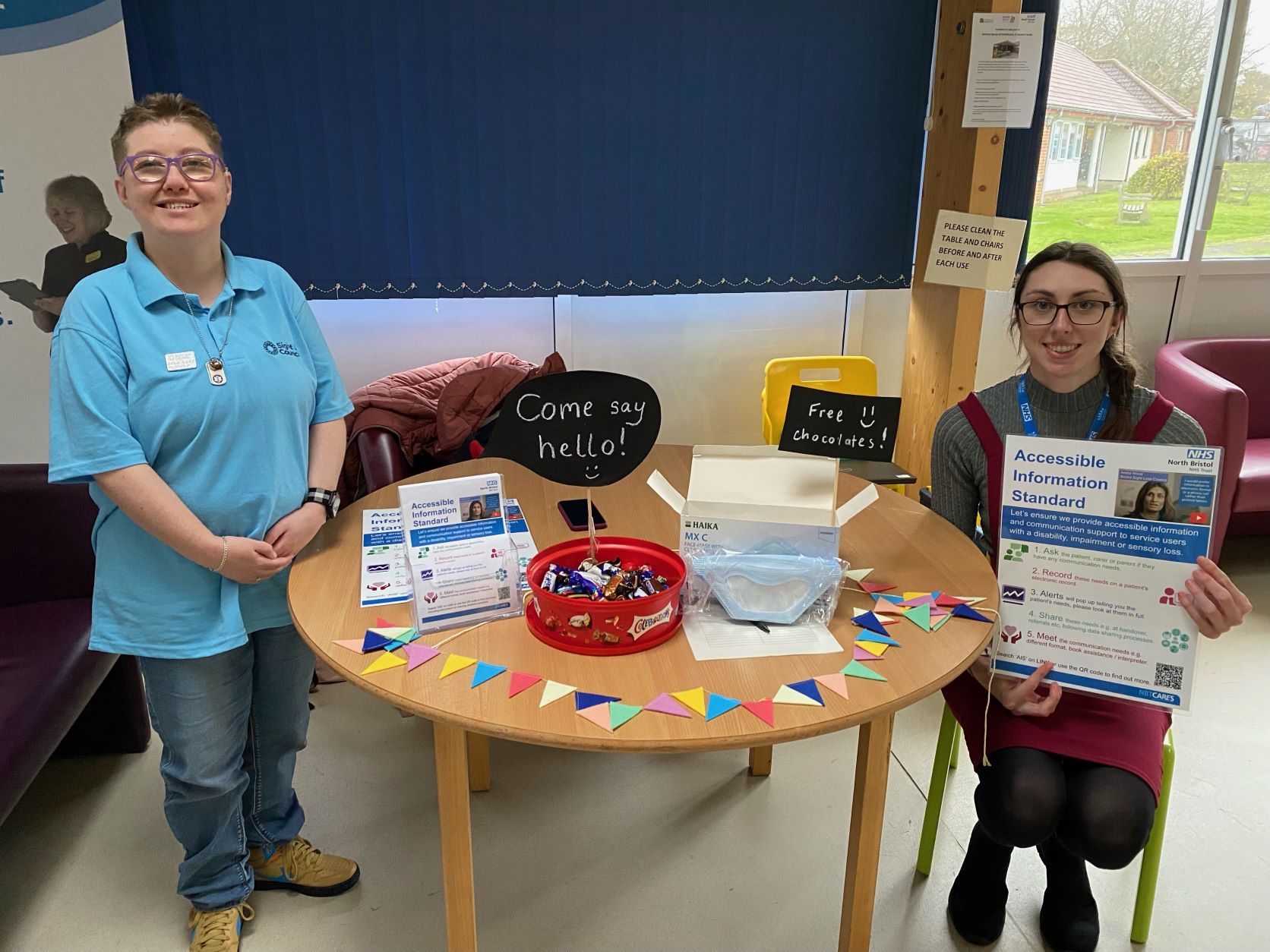 Bristol Sight Loss Council member Emma with North Bristol NHS Trust (NBT) staff member Rosie at a table with information on AIS in NBT Maternity.