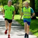 Image shows Danny Clark, Greater Manchester SLC member, running with a sighted guide, They are both wearing high-vis jackets.