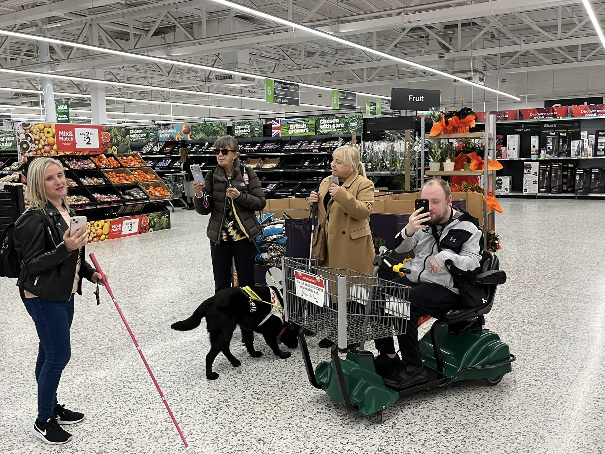 Kelly Barton and Merseyside SLC members are stood in ASDA/ They are each holding their phone up, using the GoodMaps app.