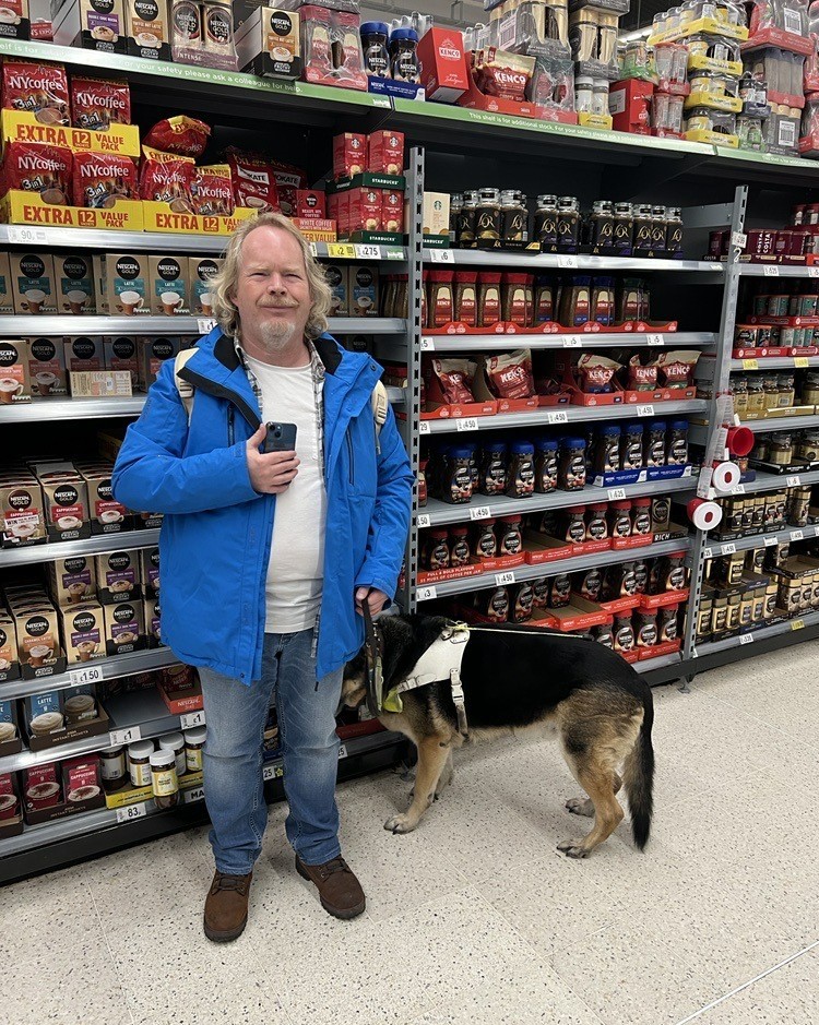 Steve Keith, Birmingham SLC member, standing in the coffee aisle with his guide dog.