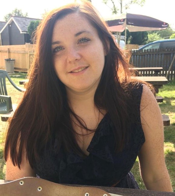 Headshoto f Samantha Leftwich, Engagement Manager for Bedfordshire SLC. She is sitting outside, looking at he camera, smiling. She has long dark hair and is wearing a black top.