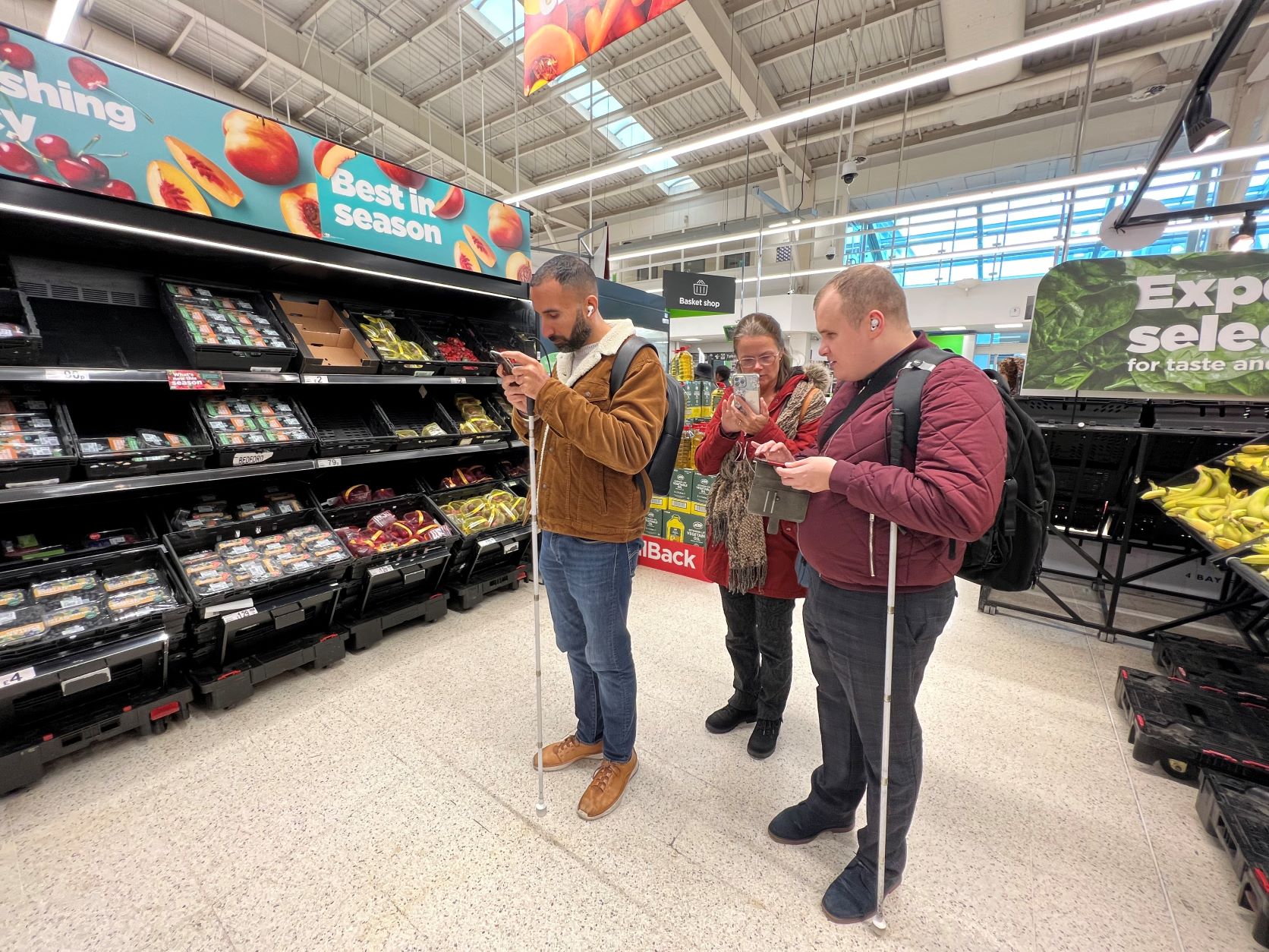 London SLC members are seen in the fruit aisle. They are all looking at their phones, using the GoodMaps navigation app.
