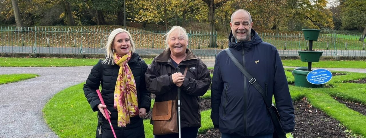 Engagement Manager Kelly Barton, with Sight Loss Council members Norma and Mick stood in Birkenhead Park. Greenery can be seen behind them.