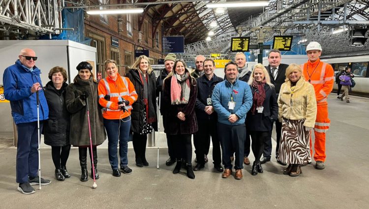 Network Rail staff and Bristol Sight Loss Council members, joined by Thomas Pocklington Trust staff, stood in a line near a platform at Bristol Temple Meads railway station. They are facing the camera and smiling.