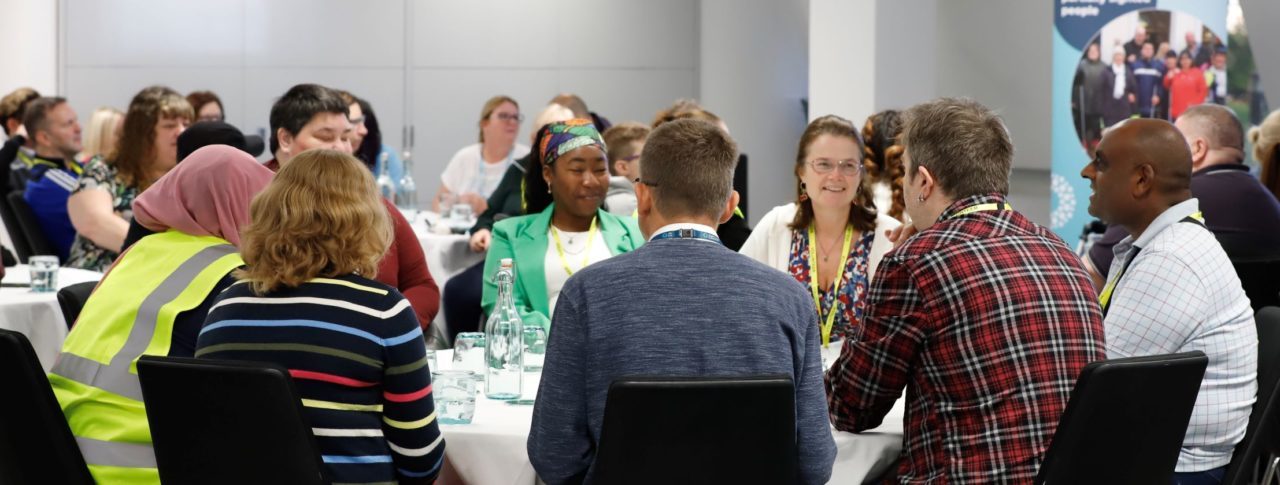 Sight Loss Council volunteers sat around a table having a discussion at a recent conference. A Sight Loss Council banner is in the background.