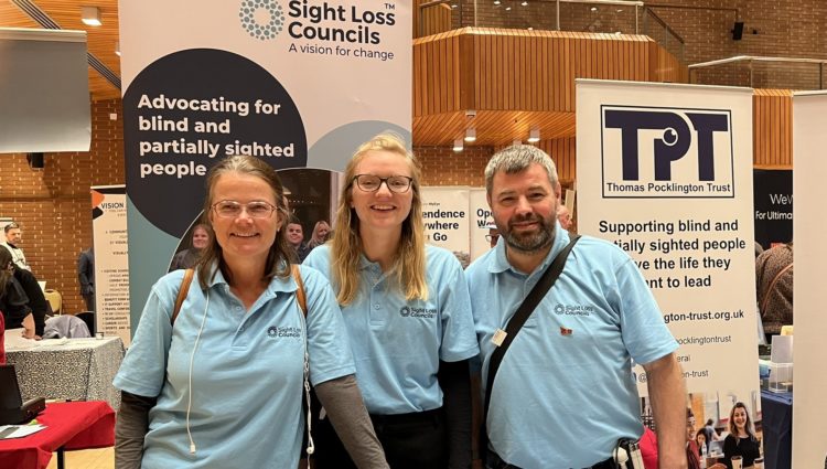 Image shows London SLC members Vicky and Steve with Senior Engagement Manager Lucy. They are behind a stall and infront of a Sight Loss Council and Thomas Pocklington Trust banner.