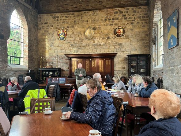 Iain Mitchell, Senior Engagement Manager for the North, is opening the 'Enable us to enable you' event at Bedern Hall. Delegates are sat around tables in the medieval dining hall. There are shields and paintings hanging on the stone walls