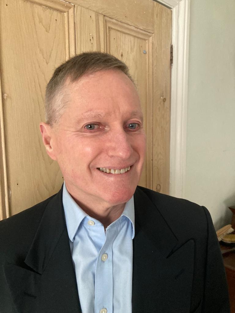 Image shows South West London SLC member, Harry Meade. He has his head turned to the camera and is smiling. he is standing in front of a door, smiling.