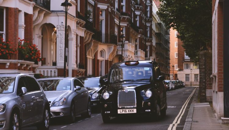 Image shows a black cab driving down a residential street in south-west London alongside a row of tall, grand, Victorian houses.