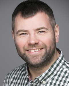 Headshot of Steven reed, London SLC member. He is looking at the camera smiling. he is wearing a navy blue and white checked shirt.