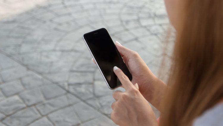 Close up on a woman's hand, holding a smartphone. Her hand finger is touching the screen. The right hand side of the image is framed by her long, red, hair.