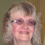 Image shows Heather Armstrong, Bristol SLC member. She has shoulder length hair and is wearing glasses and a beaded necklace. she is smiling at the camera.