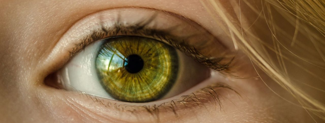 Close up of an eye with a green iris. Blonde hair is seen skimming the person's forehead.