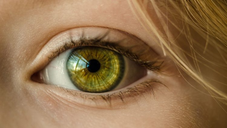 Close up on an eye with a green iris. Blonde hair is seen skimming the person's forehead.