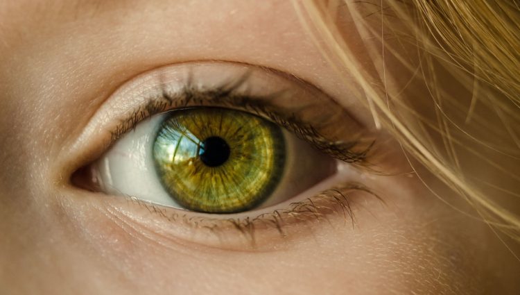 Close up of an eye with a green iris. Blonde hair is seen skimming the person's forehead.