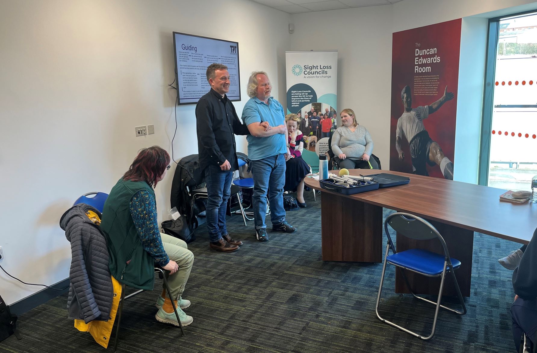 Martin Symcox, Head of Sport & Development at TPT, is standing at the front of the room with SLC member, Steve. They are demonstrating how to guide someone.