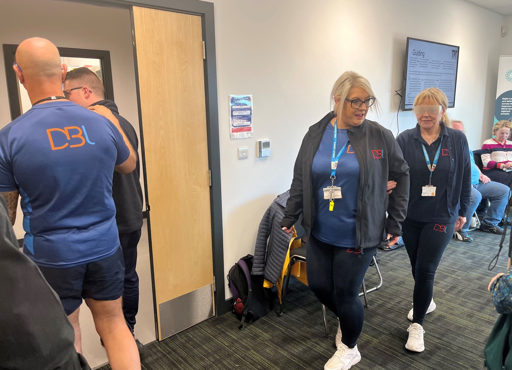 Staff from Duncan Edwards leisure centre are participating in a sighted guiding exercise. One person is guiding, the other is wearing sim specs.