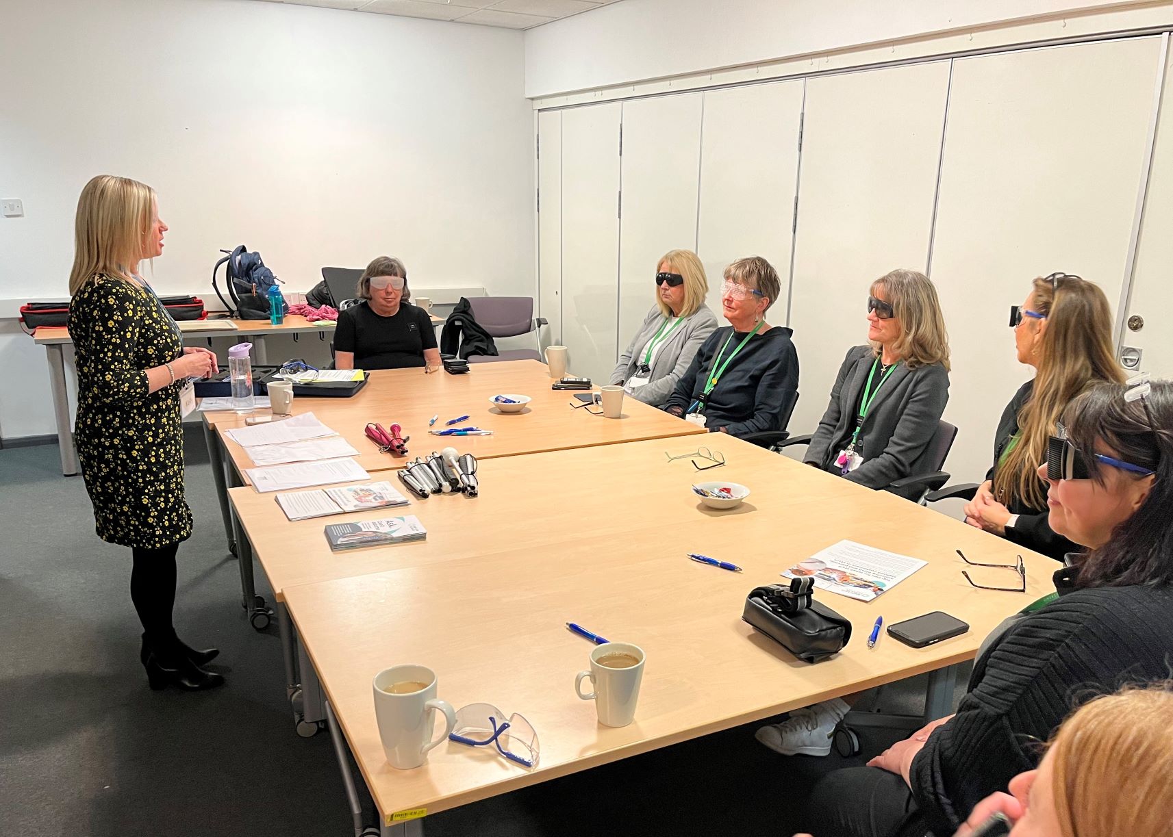 Image shows Kelly Barton, EM for Greater Manchester, presenting to staff members from John Lewis. The team are all sat around a table, wearing sim specs.
