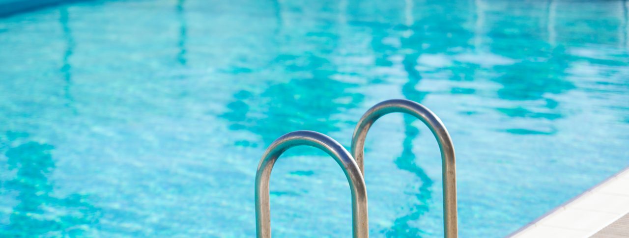 Close up image of the side of a swimming pool, with a metal ladder into the pool as the main focus.