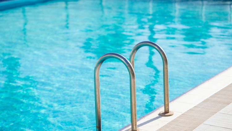 Close up image of the side of a swimming pool, with a metal ladder into the pool as the main focus.