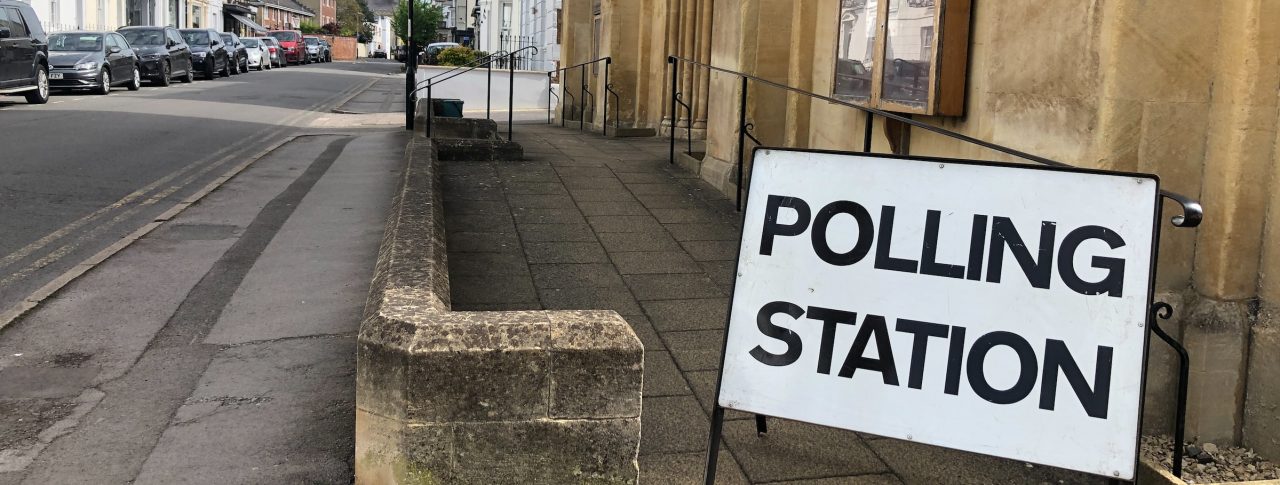 A sign reading 'Polling Station' outside a sandstone building on an urban street.
