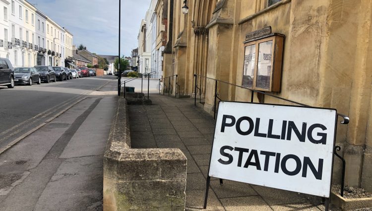 A sign reading 'polling station' outside a sandstone building on an urban street.