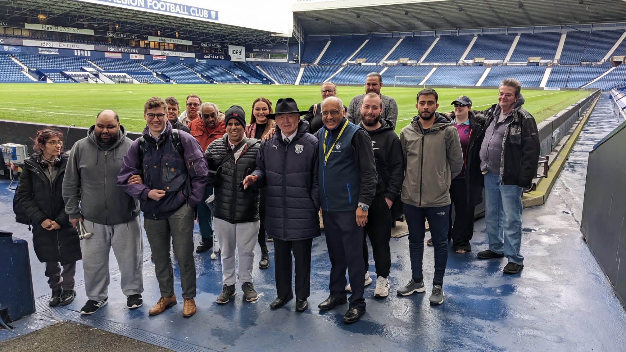 Blind and partially sighted delegates, Sight Loss Council members (Mo Azeem, Edward Jackson, Millie Hayter), Ashleigh Bryant (SLC Co-ordinator) and guest listeners James Bullen (West Midlands Motability) and Jamie Reilly (Vulnerabilities Team, University Hospitals Birmingham) all stood in front of the football pitch with tour guide, Alan Cleverley.