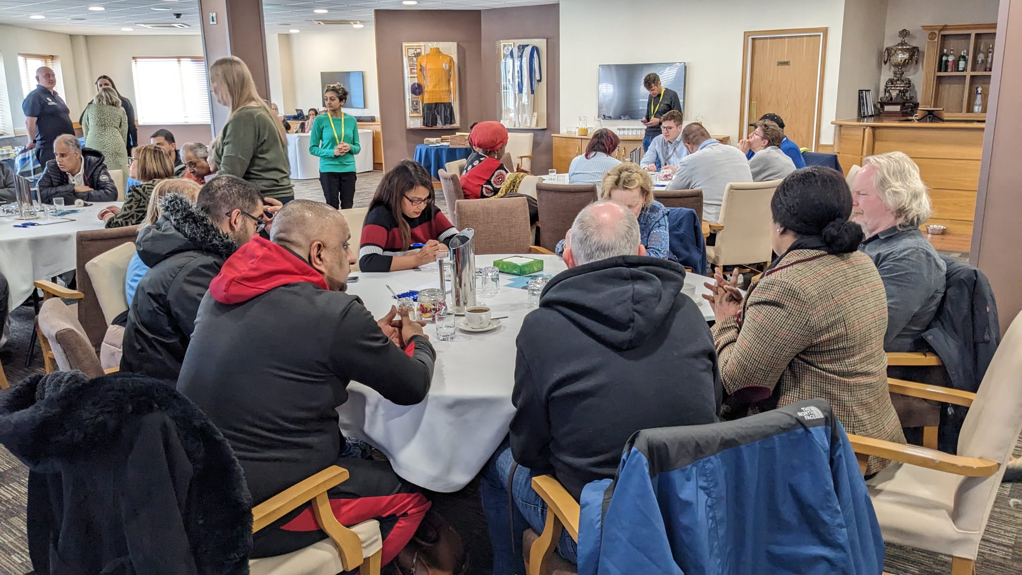 Table discussions with blind and partially sighted delegates, Sight Loss Council members and Jamie Reilly (Vulnerabilities Team, University Hospitals Birmingham). Delegates are sat around circular tables in a large room.