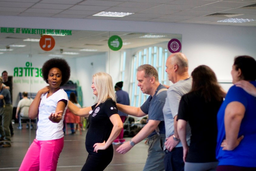 Louise, Illuminate Freedom, is leading a group of 5 men and women in a conga-style chain as part of an exercise class.