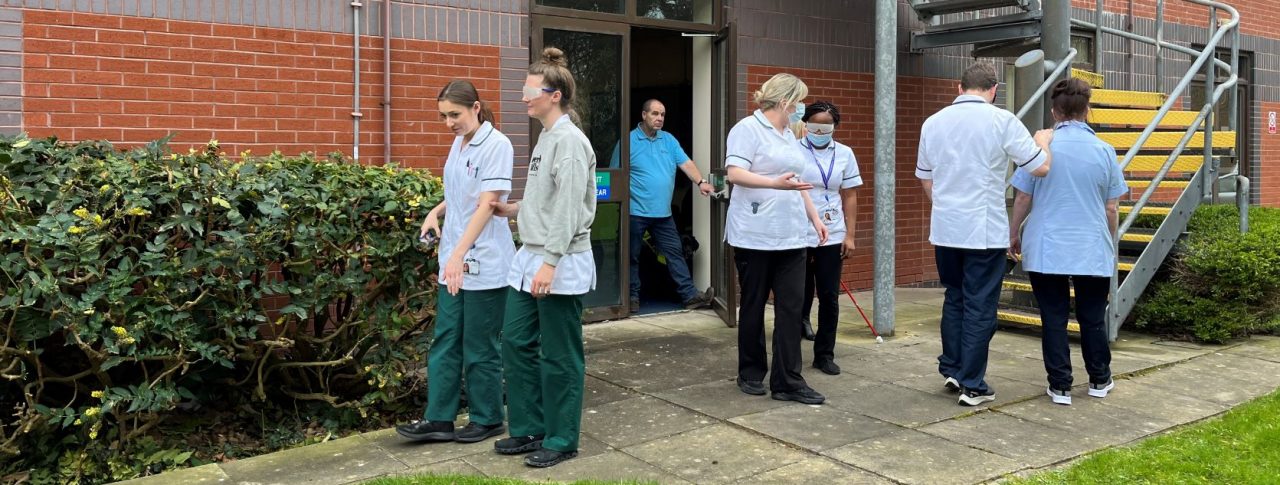 Image shows three pairs of staff members participating in sighted guide training outside.