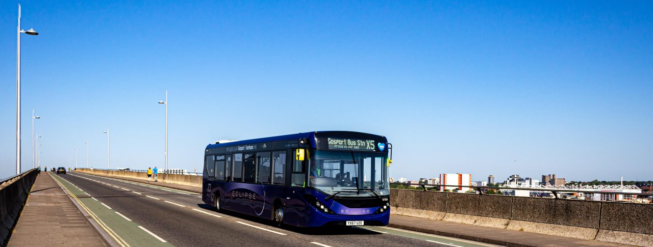 A bus bus heads across a road bridge with a blue sky in the background.