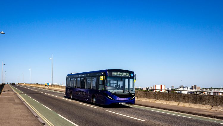 A bus bus heads across a road bridge with a blue sky in the background.