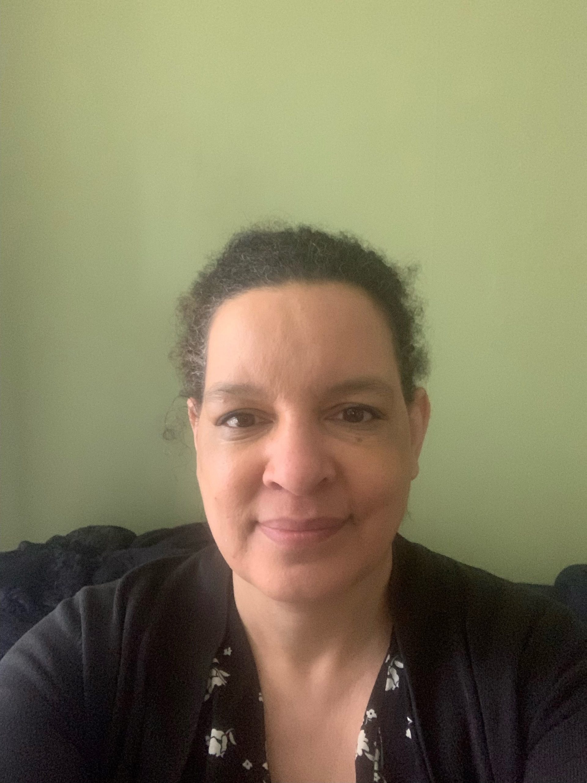 Denise, London SLC member, is seated, facing the camera, and smiling. Her hair is tied back.