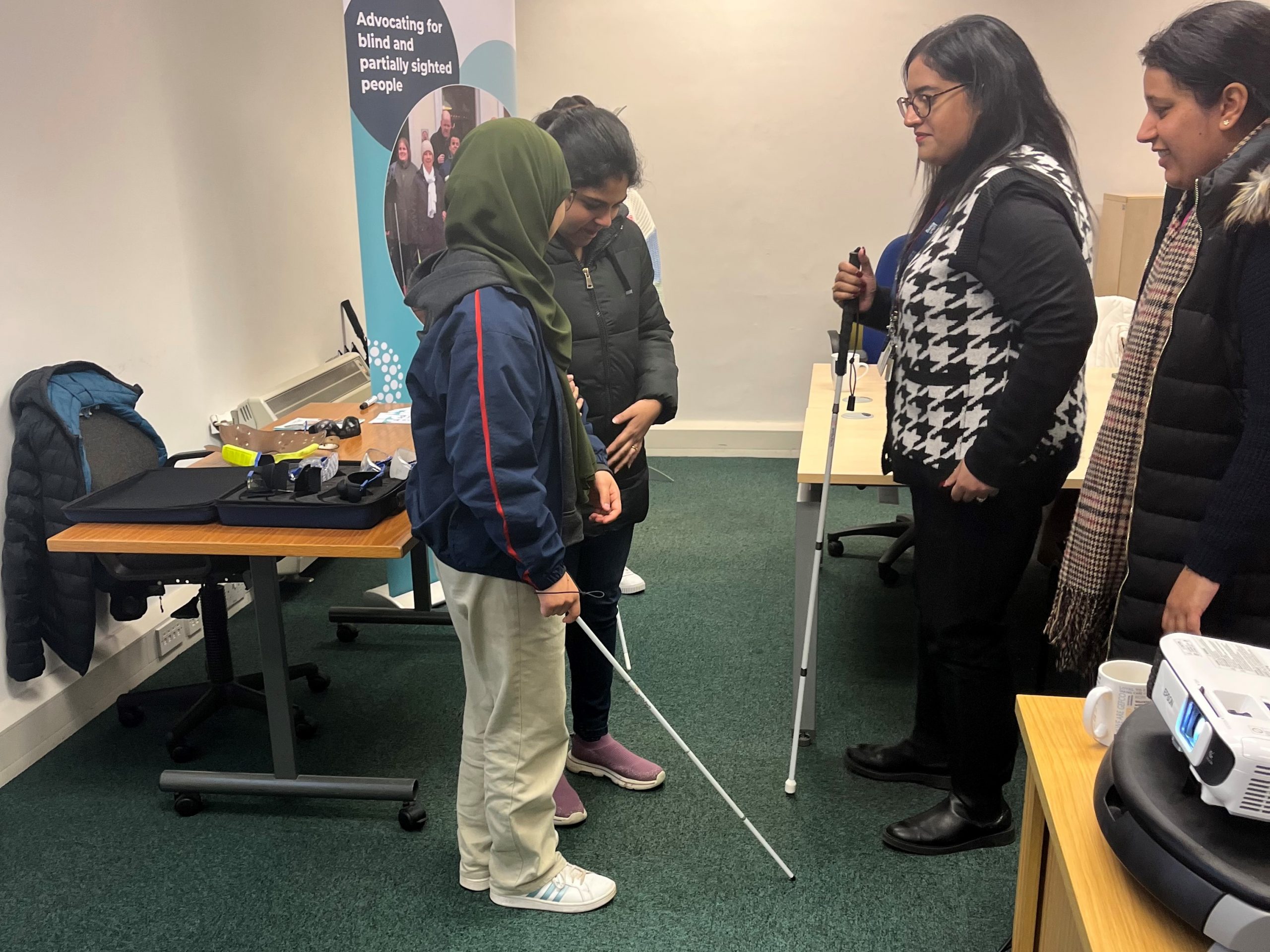 Two pairs of Ethos Farm Staff taking part in the sighted guide training. One person from each pair is holding a white cane, and being guided by the other.