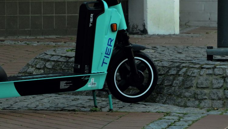 A close up of the front wheel of a TIER e-scooter. The e-scooter is turquoise, with TIER written on the frame, by the wheel.