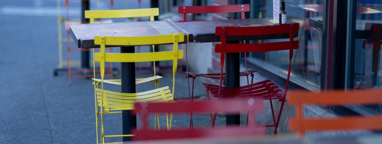 Red and yellow chairs placed on either side of a table outside a cafe.