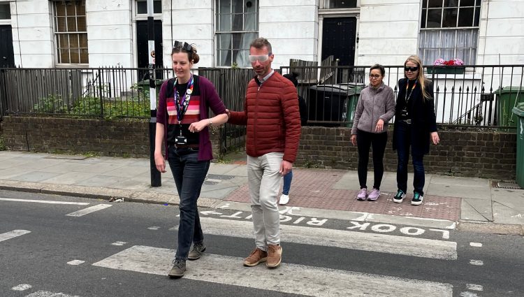 Camden Council councillors and cabinet members crossing a road at a zebra crossing during the sim spec walk. From left to right: Jenny Mulholland Camden Councillor (Gospel Oak ward), Adam Harrison, Cabinet member for a sustainable Camden and Camden Councillor (Bloomsbury ward), a My Sighted Guide Volunteer, and Sian Berry, Camden Councillor (Highgate Ward)