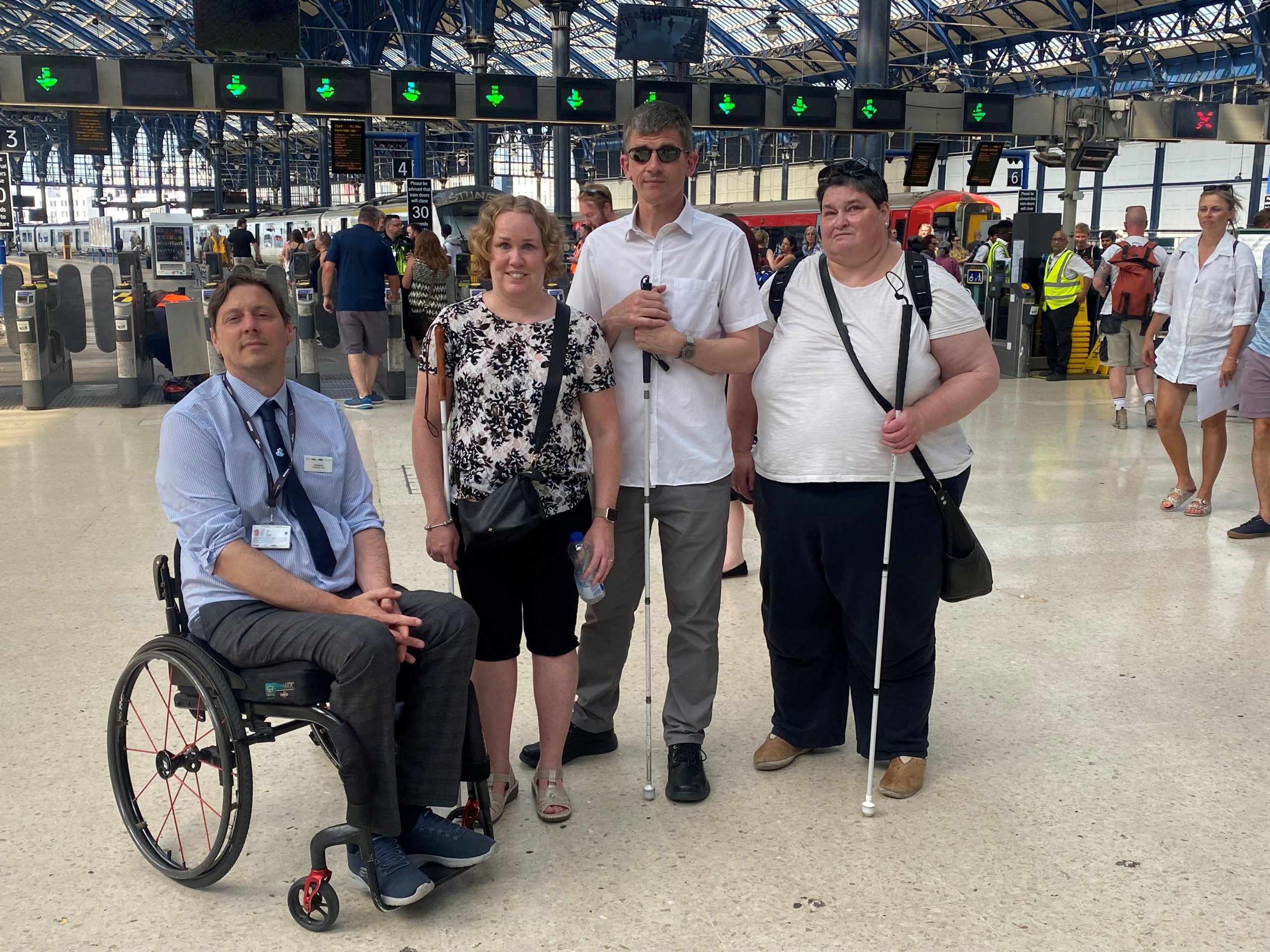 From left to right: Carl Martin, Accessibility Lead for Govia Thameslink Railways; Linn Davies, East Sussex SLC member; Dave Smith, Engagement Manager for the South East, and Iris Keppler, East Sussex SLC member. They are in the concourse of Brighton train station, looking at the camera, smiling.