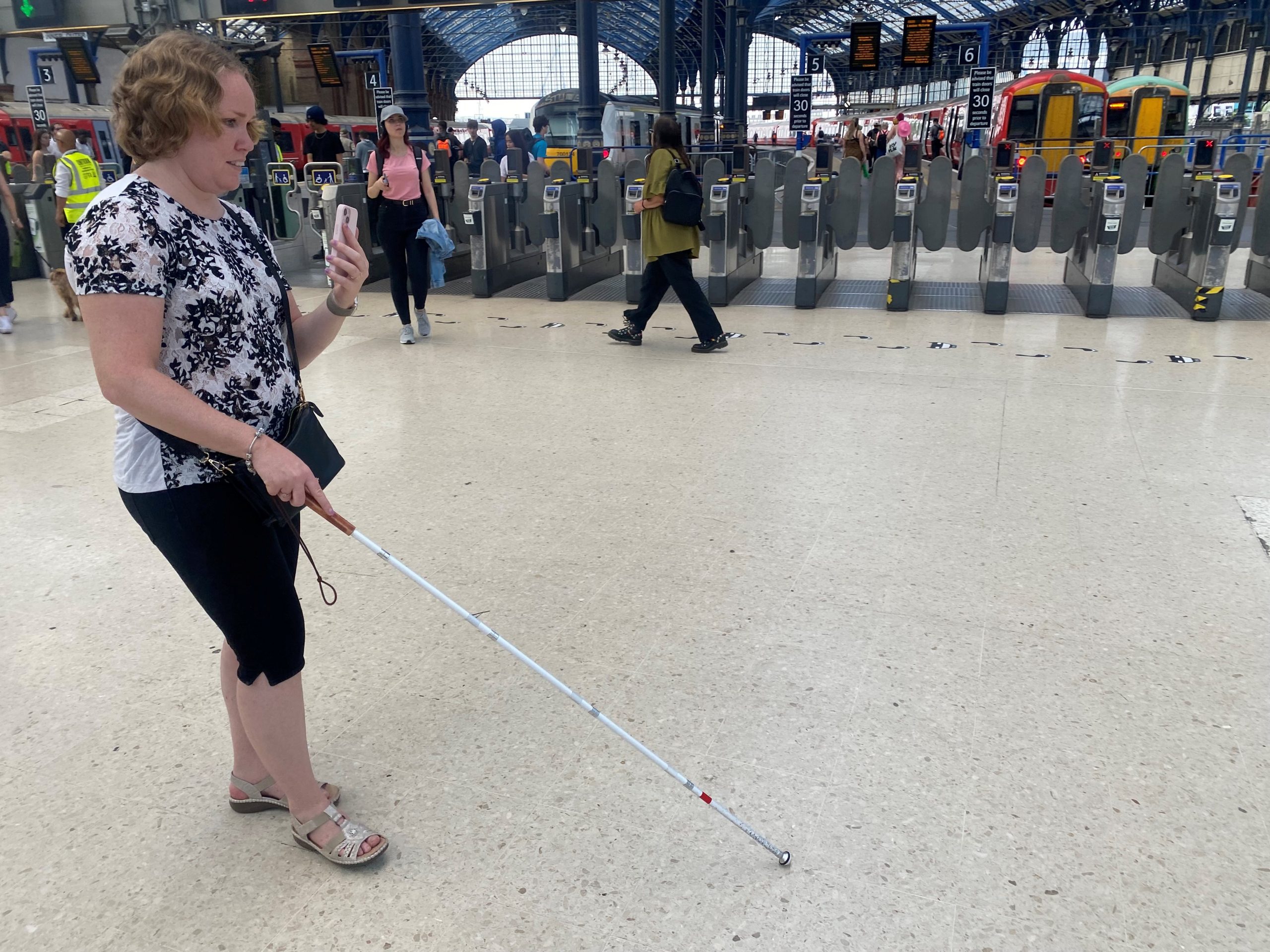 East Sussex SLC member, Linn, is being guided through Brighton train station whilst using the Aira app. The ticket barriers to the platforms are shown in the background.