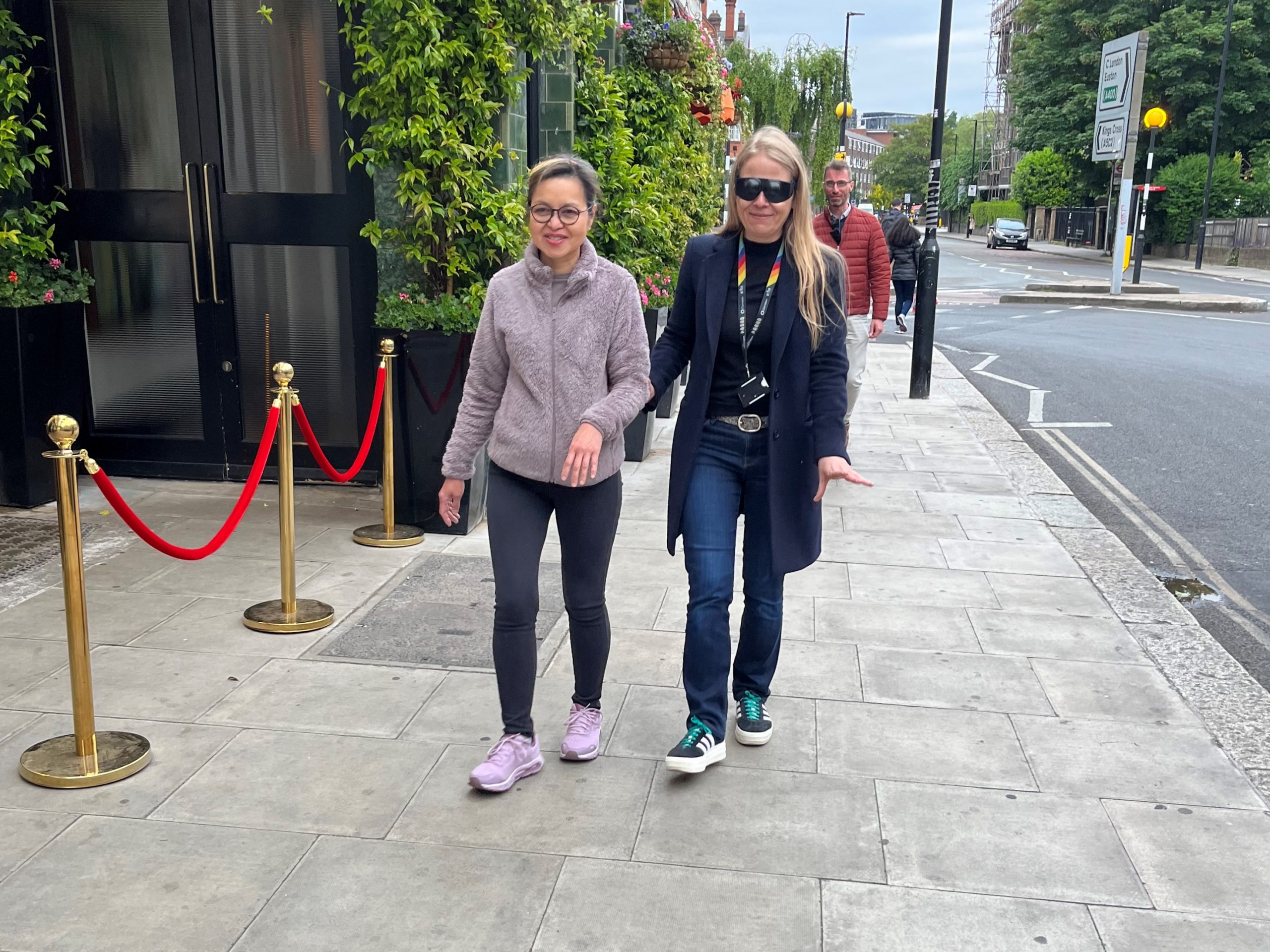 Sian Berry, Camden Councillor (Highgate Ward), being guided down the street by a My Sighted Guide volunteer during the sim spec walk. Sian is wearing a pair of sim specs.