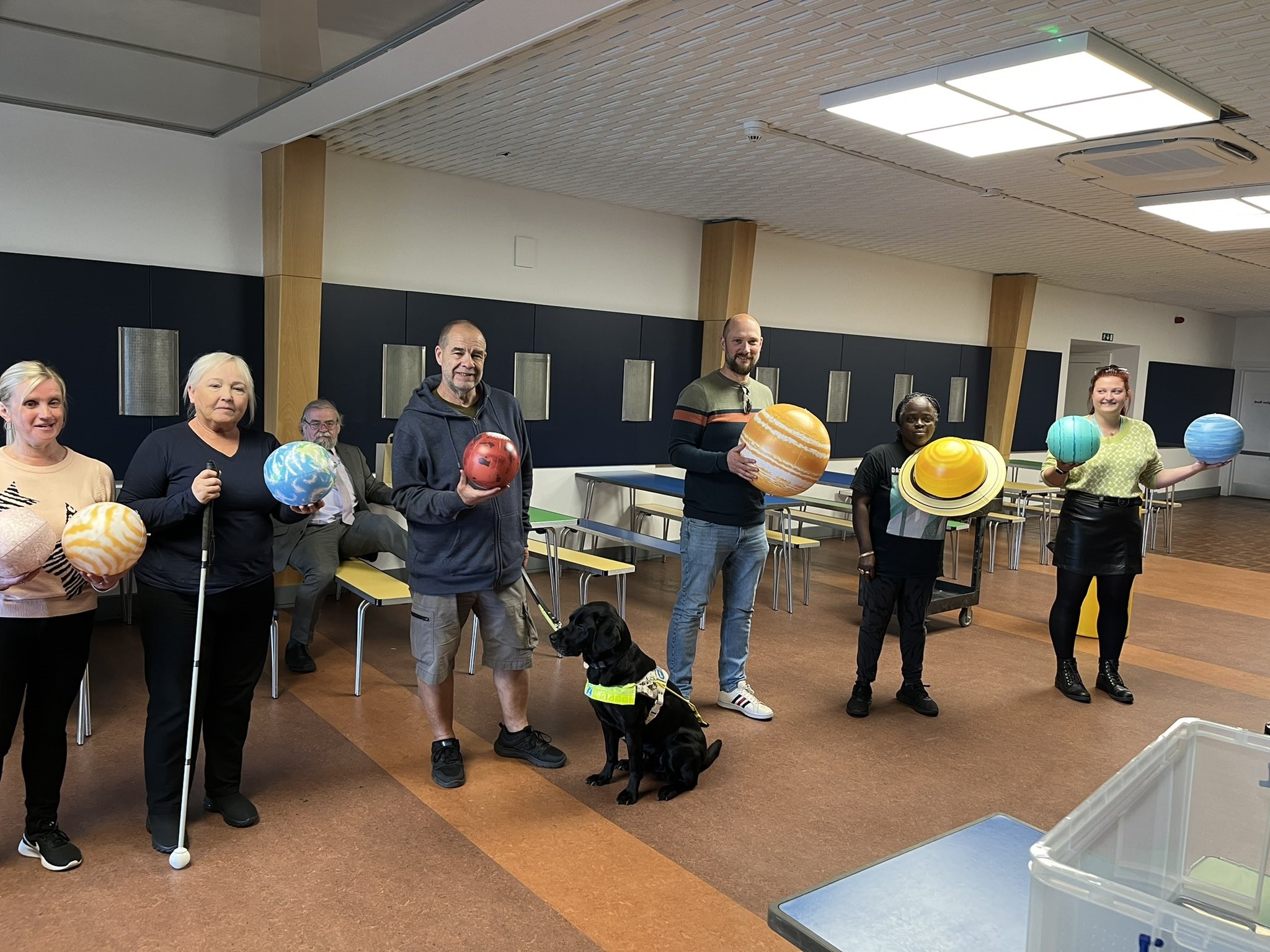 Merseyside SLC members standing in a line, each holding a model planet. From left to right: Kelly Barton, Norma Williams, Mick Spriggs, and Naomi Ditchfield. Megan and another staff member are also shown in the photo holding planets.