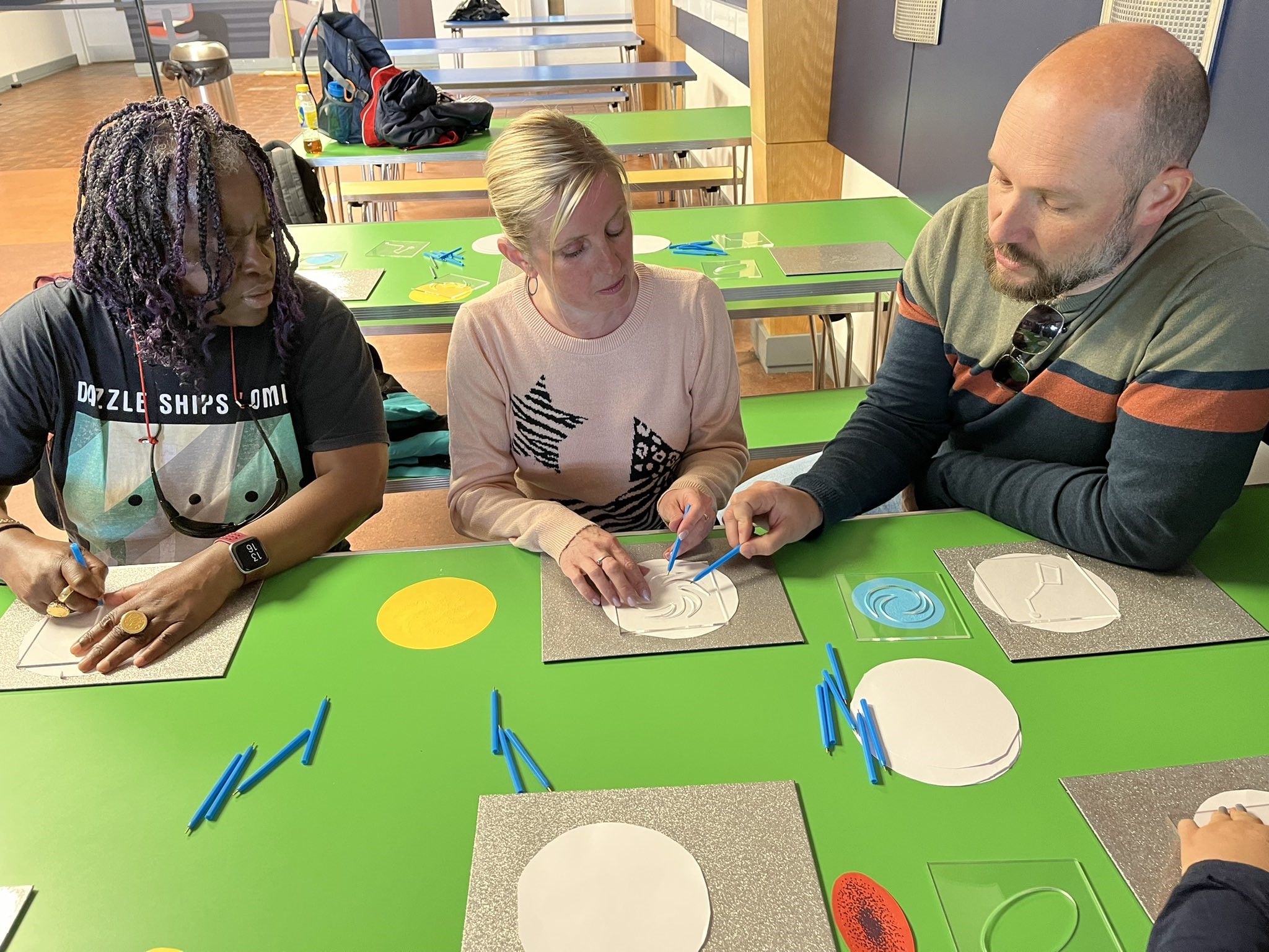 Naomi Ditchfield, Kelly Barton, and Steve Bignell are sat down at a table, creating their own galaxies by stencil.