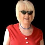 Headshot of Nottinghamshire SLC member, Caroline Wootton. She is standing against a black background, and smiling at the camera. She is wearing a red top and sunglasses.