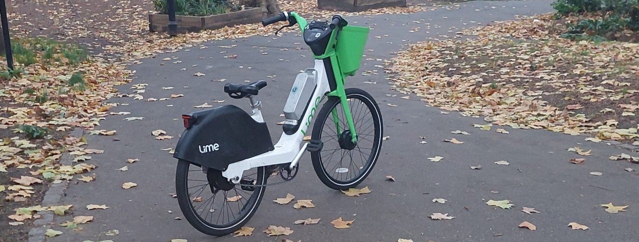 An abandoned Lime e-bike, in the middle of a path in a park.