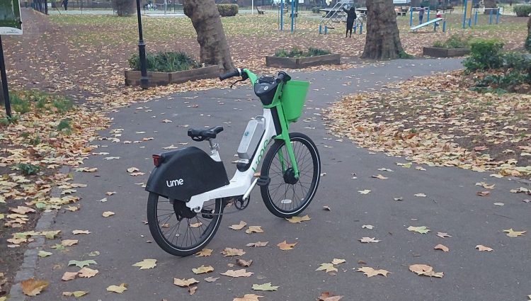 An abandoned Lime e-bike, in the middle of a path in a park.